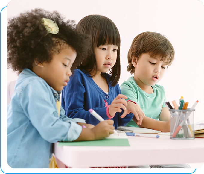 Three children are sitting at a table and writing.