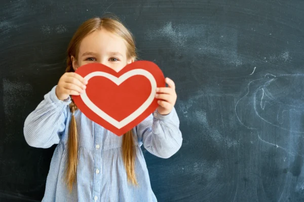 A little girl holding up a heart shaped sign.